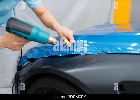 Autoverpackung, Mechaniker mit Trockner installiert Schutzfolie oder Folie auf Fahrzeughaube. Arbeiter macht Auto-Details. Autolackschutz coa Stockfoto
