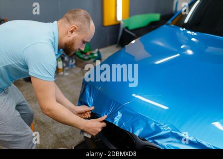 Autoverpackung, Mann mit Rakel installiert schützende Vinylfolie oder Folie auf der Haube. Arbeiter macht Auto-Details. Automobil-Lackschutzbeschichtung, prof Stockfoto