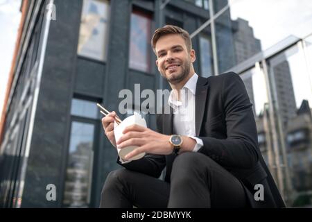 Lächelnder Mann, der auf der Treppe sitzt und asiatisches Essen isst Stockfoto