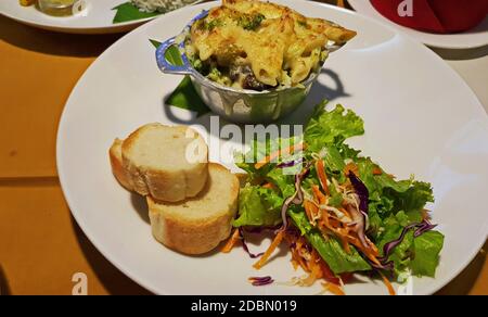 Gebackene Julienne, Scheiben Baguette, gehackter Salat. Essen auf einem weißen Teller Stockfoto