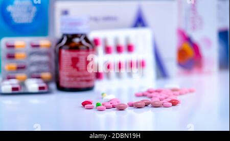 Tabletten und Kapseln Pillen auf verschwommene Drogenflasche, Kapsel in Blisterpackung und Papierkarton Packung Medizin. Rosa und rote Tabletten und grün-gelbe Kappe Stockfoto