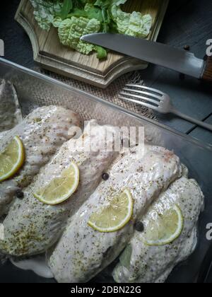 Marinierte Putenflügel in einem Tablett auf einem Holztisch, für das Braten im Ofen vorbereitet. In der Nähe gibt es Gewürze und Kräuter. Stockfoto