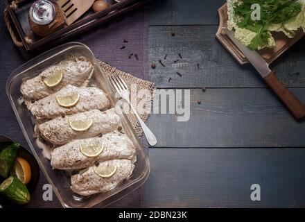 Marinierte Putenflügel in einem Tablett auf einem Holztisch, vorbereitet für das Braten im Ofen. Es gibt Gewürze und Kräuter in der Nähe. Draufsicht, Kopierbereich. Stockfoto