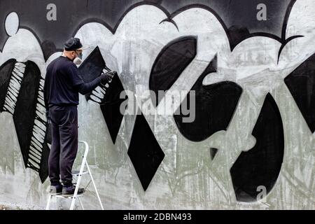 Graffiti-Künstler in Aktion, auf Leitern stehend und mit Schutzmaske / Atemschutzmaske mit Filtern. Abstrakte Zeichnung mit Sprühfarbe in einer Dose. Stockfoto