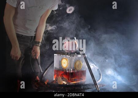 Ein Mann lässt Rauch aus einer Shisha in Form von Ringen. Foto ohne Gesicht auf dunklem Hintergrund. Nicht fokussiert. Das Konzept der schlechten Gewohnheiten. Stockfoto