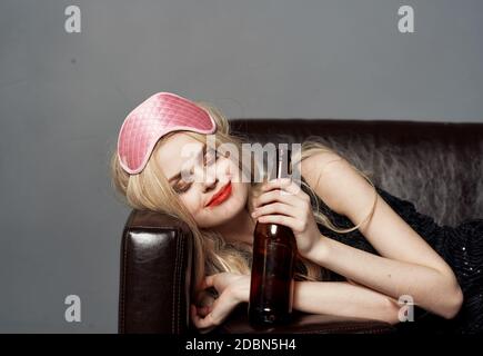 Eine Frau mit einer rosa Maske auf dem Kopf und Eine Flasche Bier schläft auf der Couch Stockfoto