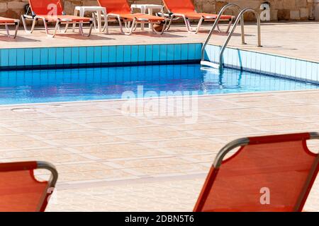 Swimmingpool mit leeren Sonnenliegen außerhalb des Urlaubshotels. Zeitgenössische Entspannung blauen Wasserpool Fotografie. Pool mit Leiter und Liegestühle in Stockfoto