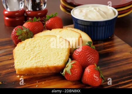 In Scheiben geschnittener Kuchen, frische Erdbeeren und Schlagsahne auf einem Schneidebrett Stockfoto