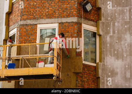Gerüst in der Nähe eines im Bau befindlichen Hauses für externe Gipsarbeiten. Modernes Apartmentgebäude in der Stadt mit Steinbalkons. Stockfoto