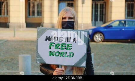 Made in a free world - Slogan auf Protestaktionen in der Stadt. Junge blonde Frau in Schutzmaske zu Fuß mit Dampfer. Stockfoto