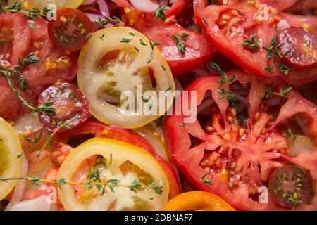 Eine Auswahl an geschnittenen Tomaten aus Erbstück, die mit Weißweinessig und Olivenöl-Dressing, geschnittenen roten Zwiebeln und frischem Thymian serviert wurden. Engl Stockfoto