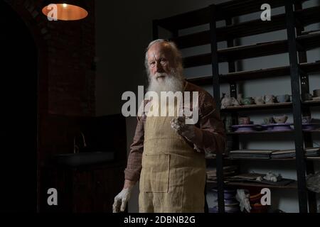 Ein junger männlicher Töpfer ist in seiner Werkstatt auf einem Töpferrad im Handwerk beschäftigt und stellt ein Tonprodukt her Stockfoto