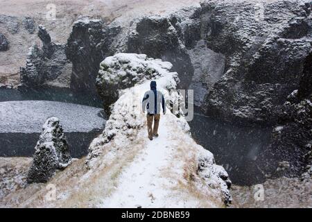 Junger Mann in blauer Jacke, der in Südisland auf einem Bergrücken des Fjaðrárgljúfur-Canyons schneit. Stockfoto