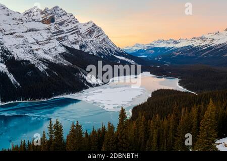 Die Sonne untergeht und der Himmel leuchtet mit Farbe über einem eisbedeckten Peyto-See im Banff-Nationalpark. Stockfoto