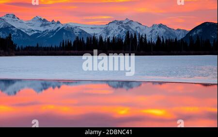 Die Sonne geht auf und leuchtet mit Farbe über einem eisbedeckten Vermillion Lake im Banff National Park. Stockfoto