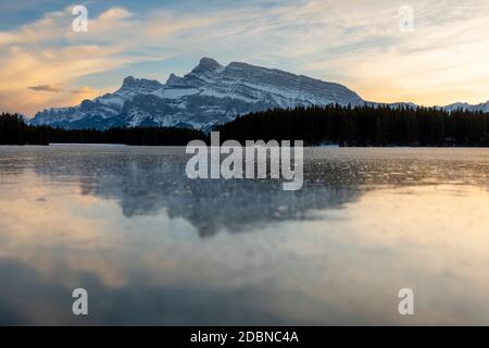 Die Sonne geht unter und leuchtet mit Farbe über Mt Rundle und einem Eis bedeckt zwei Jack Lake im Banff National Park. Stockfoto