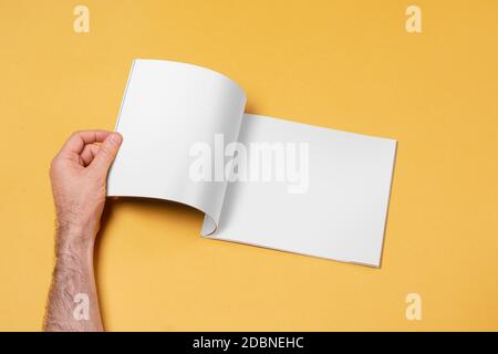 Männliche Hand öffnete einen Katalog auf gelbem Hintergrund, editierbare Modell-up-Serie Vorlage bereit für Ihre Design-Seiten Auswahl Pfad enthalten Stockfoto
