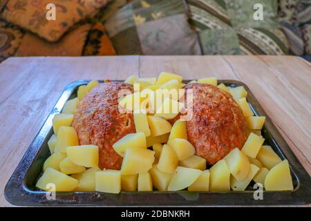Gebackenes Schweinehackfleisch und Kartoffeln auf einer schwarzen Backform. Hausgemachte Fleischschnitzel mit Kartoffeln in einer gusseisernen Pfanne auf einem Holztisch serviert. Lecker und lecker Stockfoto