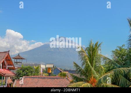 Tropisches Paradies mit Palmen und majestätischen Vulkan im Hintergrund. Weiße Wolken um ein Vulkankrater. Blick von oben über den Dächern des Hauses Stockfoto