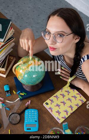 Geografie-Unterricht. Ein junges Teenager-Mädchen sitzt an einem Schulschalter. Der beste Schüler in der Schule. Interessante Geographie Lektion über unseren Planeten. Stockfoto