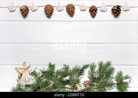 Girlande mit Zapfen und Engeln auf der Oberseite, Kiefernäste mit hölzernen Ornamenten auf weißem Holzhintergrund. Vorlage für Neujahrskarte, Platz zum Kopieren Stockfoto