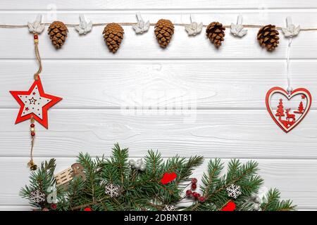 Girlande mit Zapfen und Engeln, rote Stern- und Herzverzierungen, Kiefernzweige mit Fäustlingen und Schneeflocken. Vorlage für Neujahrsposter, Platz zum Kopieren Stockfoto