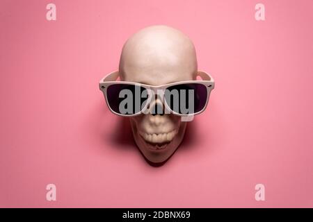 Weißer Totenkopf mit weißer Sonnenbrille auf rosa Hintergrund. Kreative minimalistische Tapete Stockfoto