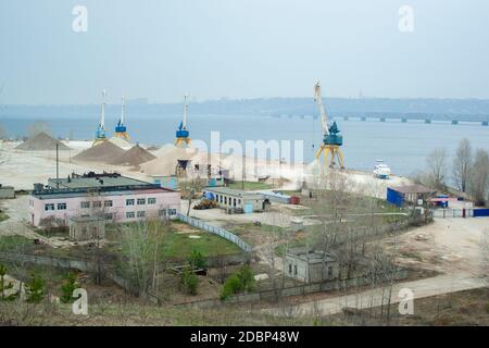 Dockkrane mit Industriegebäuden und großen Sandhaufen In der Nähe der Wolga in Russland Stockfoto