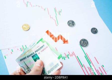 Männliche Hand, die Rubelrechnungen zum Wechselkurs des russischen Rubel und des roten Pfeils hält. Rubelabschreibung. Wechselkurs des Rubelfalls. Rubel zum Dollar Stockfoto