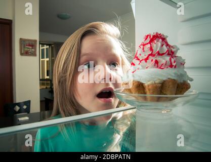 Mädchen sieht die süßen Kuchen in den Kühlschrank stellen Stockfoto