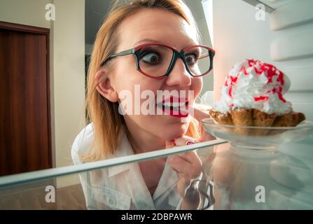 Frau sieht die süßen Kuchen in den Kühlschrank stellen Stockfoto