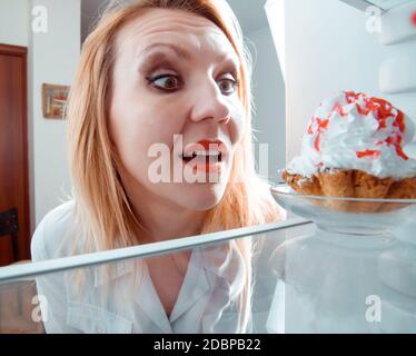 Frau sieht die süßen Kuchen in den Kühlschrank stellen Stockfoto