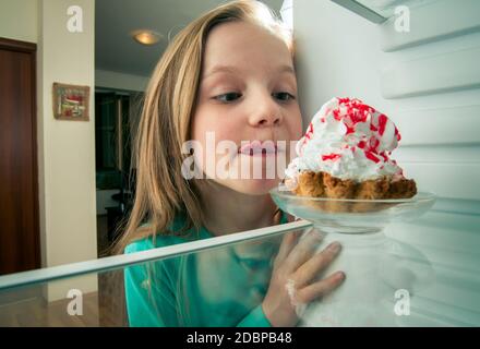 Mädchen sieht die süßen Kuchen in den Kühlschrank stellen Stockfoto