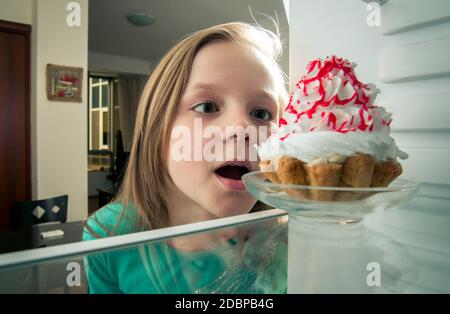 Mädchen sieht die süßen Kuchen in den Kühlschrank stellen Stockfoto