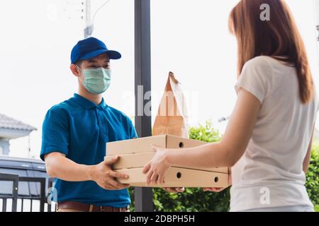 Asiatische Lieferung Express Kurier junger Mann geben Papiertüten Fast Food und Pizza-Box an Frau Kunde erhalten beide Schutzmaske Gesicht, unter Ausgangssperre Stockfoto