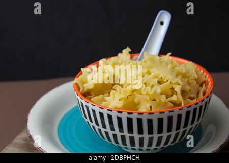 Eine Schüssel mit ungekochten italienischen kurzen Pasta als kurz bekannt mafalda auf dunklem Hintergrund mit Kopierraum Stockfoto