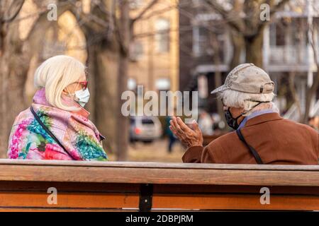 Montreal, CA - 7. November 2020: Älterer Mann und Frau mit Gesichtsmasken auf einer Bank in einem Park, während der Covid-19 Pandemie Stockfoto