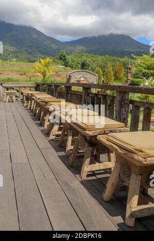 Reihe von Holzhockern mit Kissen auf der Terrasse mit Boden aus gehobelten Holzbohlen. Es stößt von grob bearbeiteten Balken. Hintergrund mit Bergen w Stockfoto