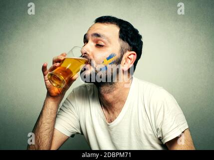 Lustig sport Fan mit Fahne gemalt auf Gesicht Bier trinken. Stockfoto