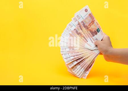 Hand hält einen Fächer aus einem 5.000-ten Russenscheine auf gelbem Hintergrund Stockfoto
