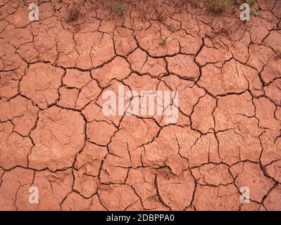 Die Risse und Spalten in der rot ausgetrockneten Erde Stockfoto