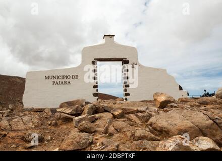 Typisches Gemeindeschild (weißes Bogentor) bei Pajara mit Wüstengebirgslandschaft im Hintergrund, Fuerteventura, Kanarische Inseln, Spanien Stockfoto