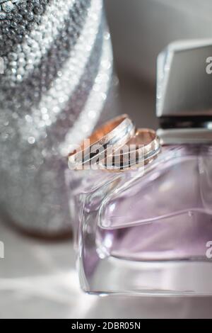 Goldene Ringe liegen auf der violetten Parfümflasche. Hochzeitstag Stockfoto