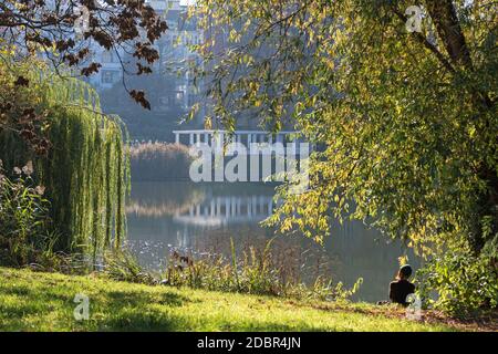 Berlin, Deutschland - 7. November 2020: Kuno-Fischer-Platz Gärten am Lietzensee mit einer jungen Frau, die den warmen Herbsttag auf dem Shor genießt Stockfoto