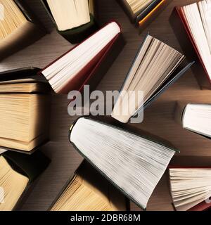 Bücher auf dem Tisch, Draufsicht. In Büchern sind die Blätter in Form eines Ventilators verteilt, die Schatten der Bücher auf einem hellen Holztisch. Zurück zur Schule. Stockfoto