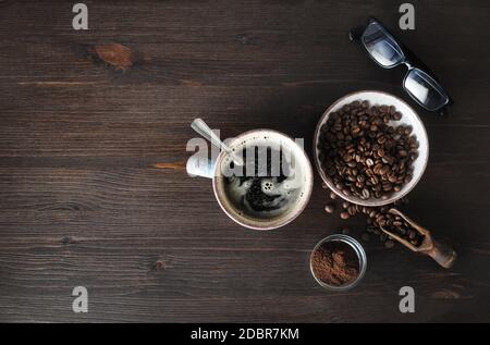 Foto von Kaffee Zutaten. Kaffeetasse, Kaffeebohnen, gemahlenes Pulver und Gläser auf Holzhintergrund. Kopieren Sie den Platz für Ihren Text. Draufsicht. Flach liegend. Stockfoto