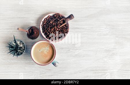 Geschmackvoller Kaffee Hintergrund. Kaffeetasse, Kaffeebohnen, Pflanzen- und gemahlenes Pulver auf hellem Holz Küchentisch. Draufsicht. Flach liegend. Stockfoto