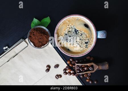 Stillleben mit Kaffee auf schwarzem Tischhintergrund. Kaffeetasse, Kaffeebohnen und gemahlenes Pulver. Flach liegend. Stockfoto