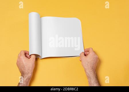 Männliche Hand öffnete einen Präsentationskatalog auf gelbem Hintergrund, editierbare Modell-up-Serie Vorlage bereit für Ihr Design, Auswahlpfad enthalten. Stockfoto