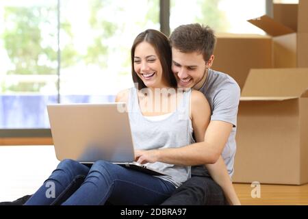 Glückliches Paar mit Laptop Umzug in ein neues Zuhause umgeben von Boxen sitzen auf dem Boden Stockfoto
